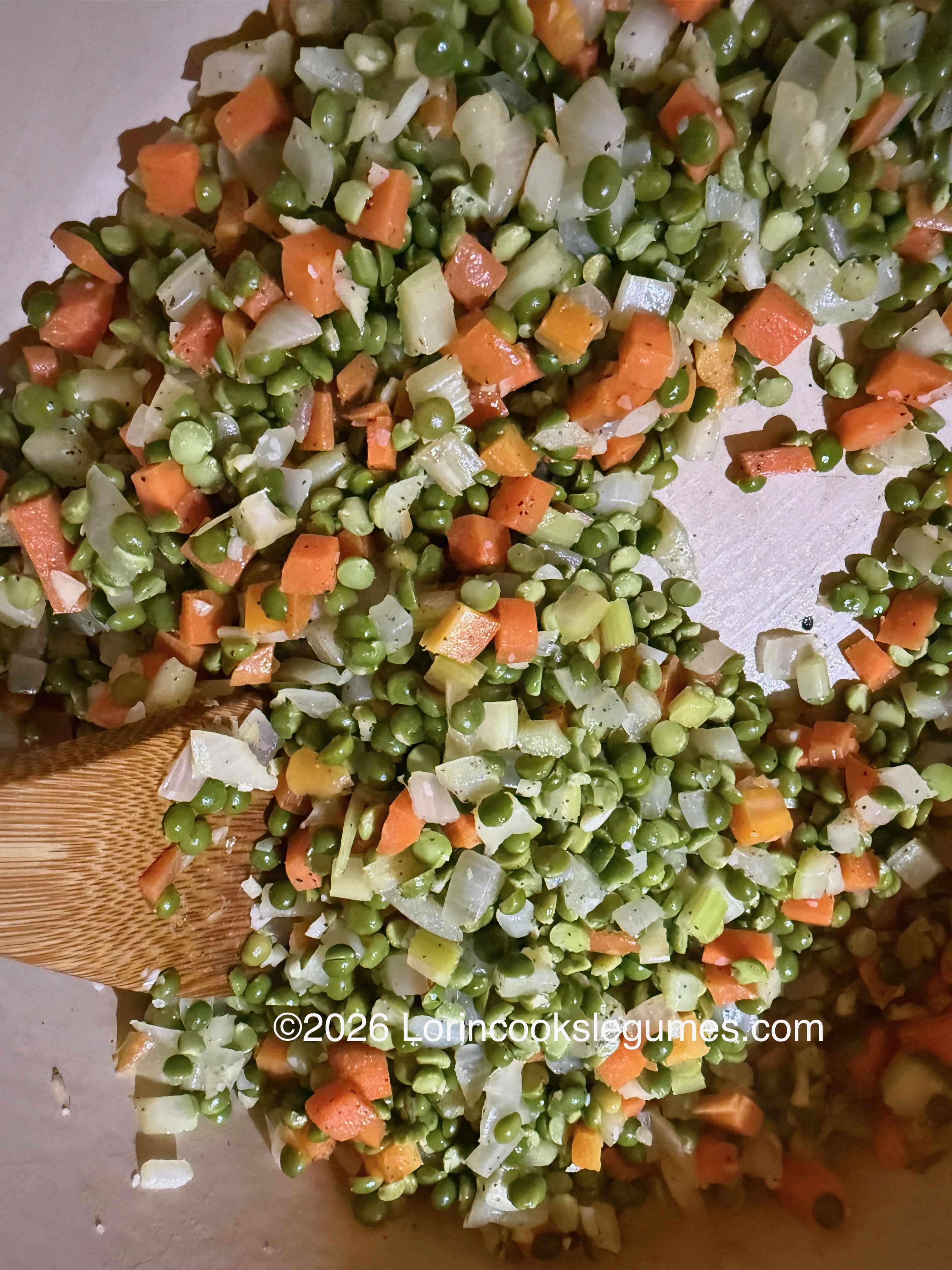 Close-up of split peas, carrots, and onions on in a light colored pot.