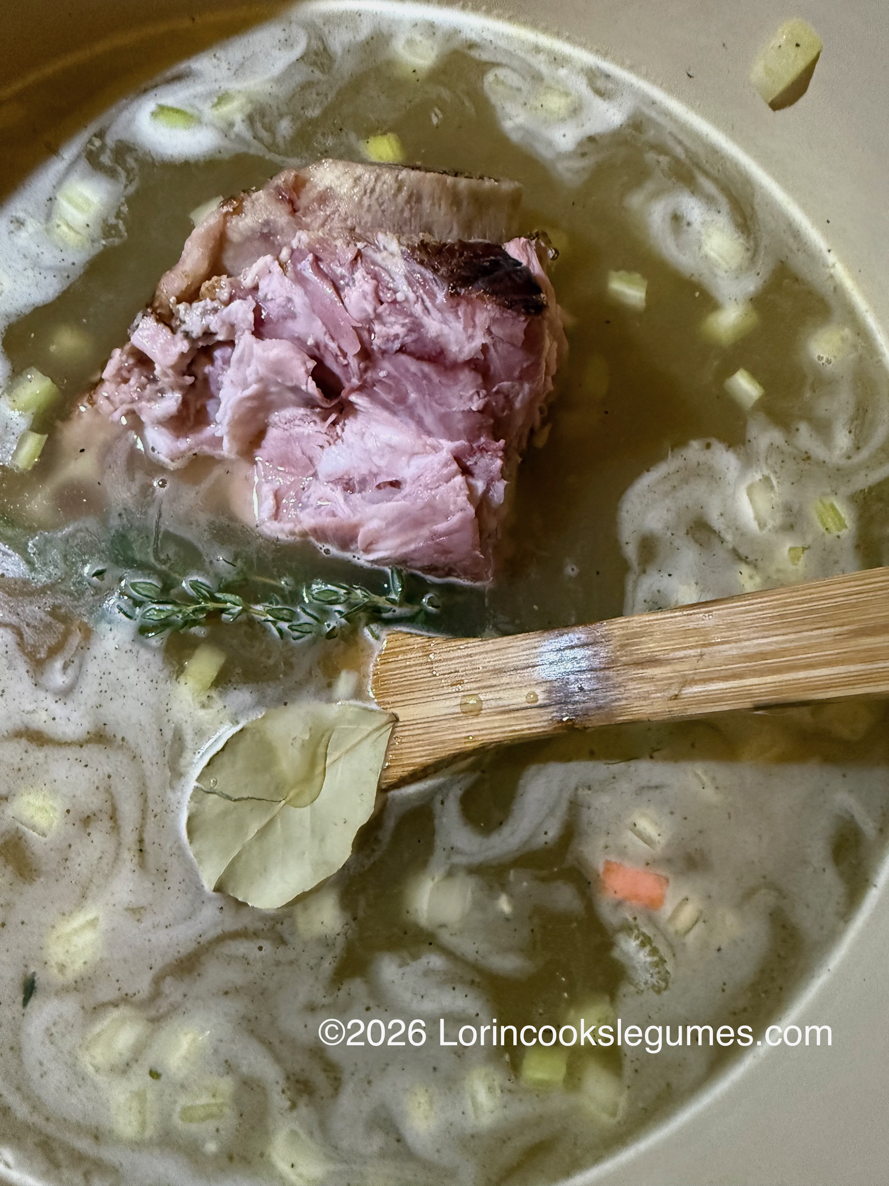 A meaty ham bone in a pot of stock with vegetables, bay leaves and fresh thyme.