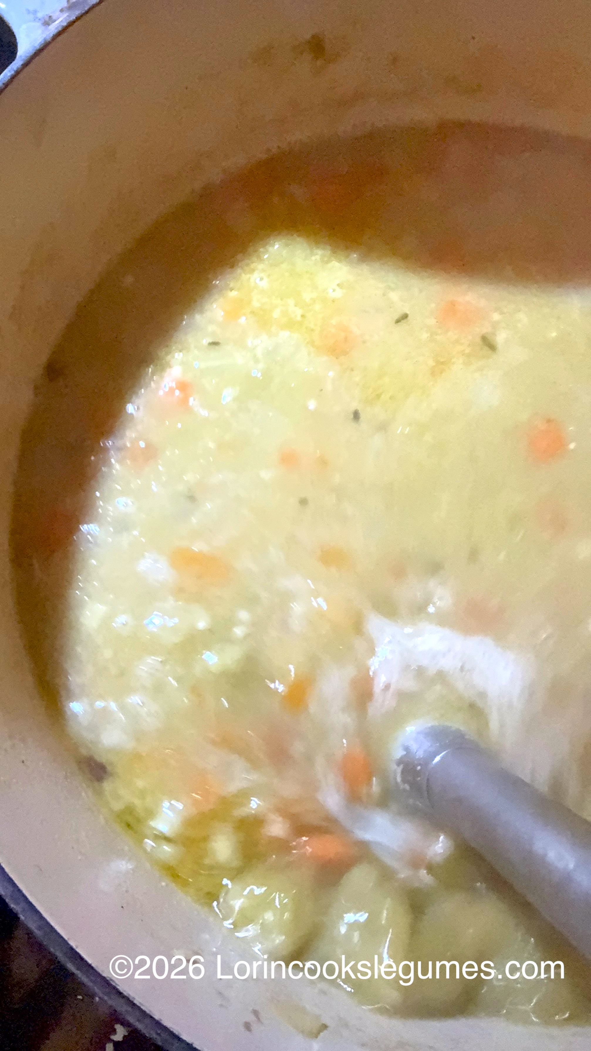 Close-up of split pea soup with carrots and herbs, being blended with a stick blender.