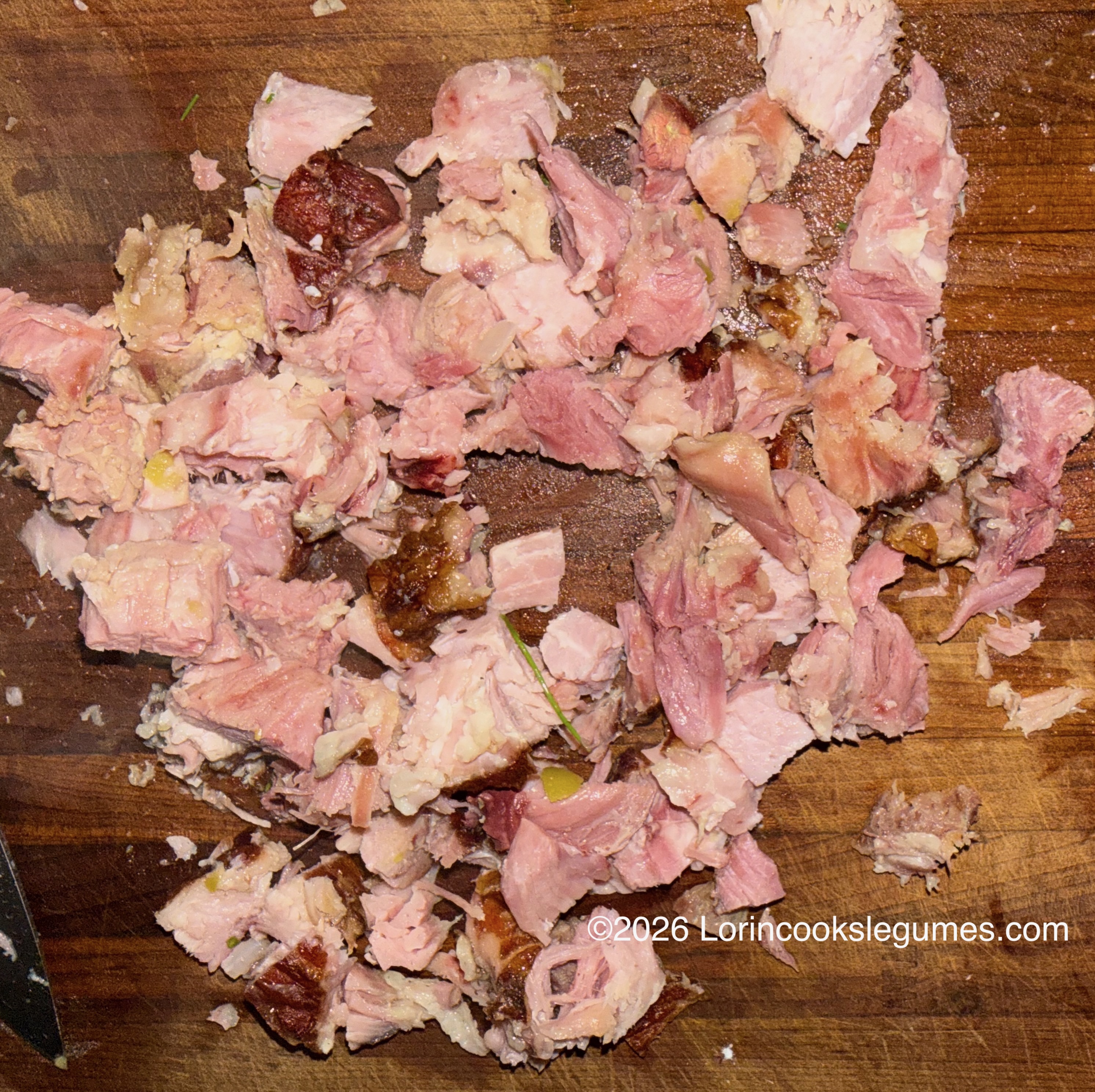 Shredded pink and browned meat with visible fat and herbs on a wooden cutting board