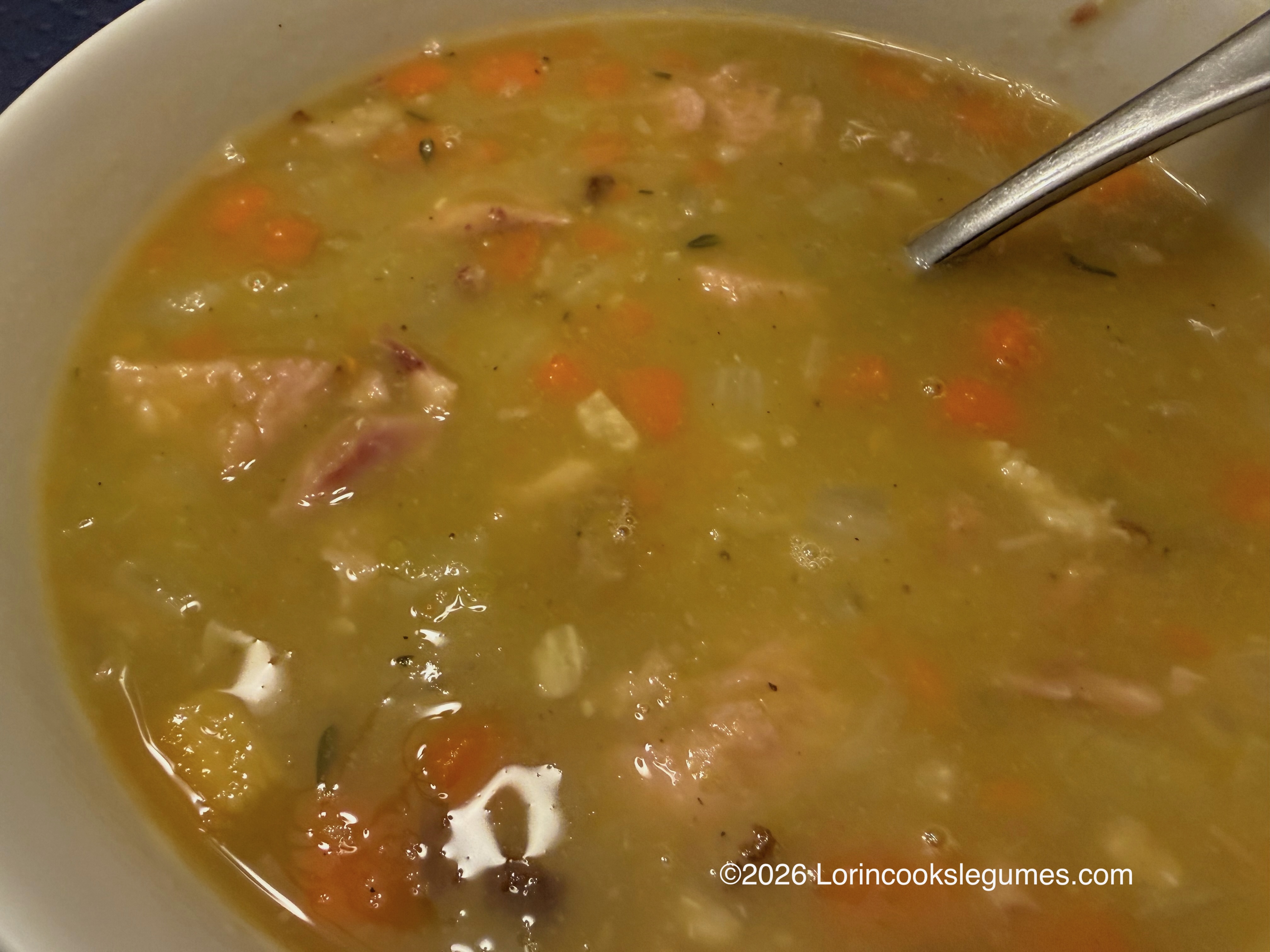 Close-up of a bowl of split pea soup with carrots and ham.